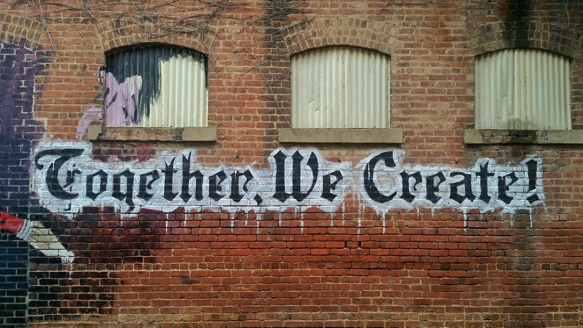 Image of graffiti over brick building saying "Together, We Create!"