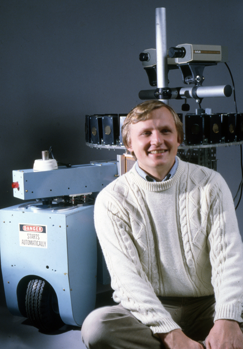 Dr. Hans Moravec, former head of the Mobile Robots Laboratory in the Robotics Institute, sits with the robot Neptune, ca. 1985. From the Robotics Institute Photograph Collection, Carnegie Mellon University Archives.