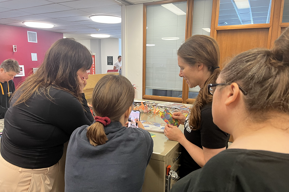 Leah Zande, Jennifer Sciullo, Anne Nowalk, Anne Kramer, and Camille Chidsey record a video of folding origami.