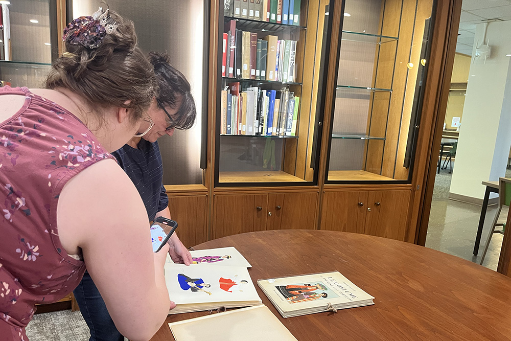 Jill Chisnell and Charlotte Trexler record a video of colorful costume prints from the collection.