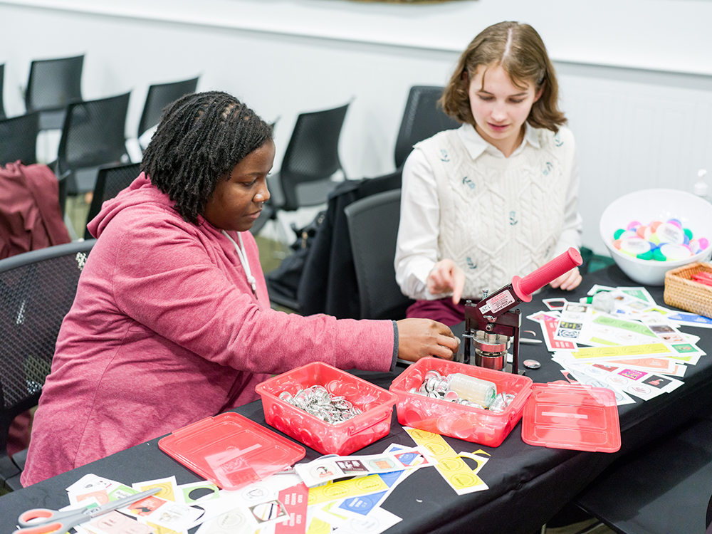 College of Fine Arts junior Moira Doolittle, the student events assistant for the Libraries, helps a guest make a button.